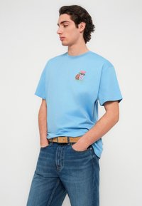 Ανοιχτό μπλε βαμβακερό T-shirt με κοντά μανίκια, με πολύχρωμο κεντημένο σχέδιο λουλουδιών και ενός μπάσκετ στο αριστερό στήθος.