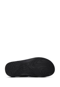 Suela de zapato de goma negra con un patrón de banda de rodadura distintivo, que presenta surcos curvados y una superficie texturizada para un agarre adicional.