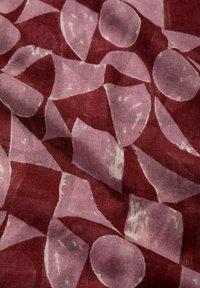 Tessuto con uno sfondo color bordeaux e forme irregolari di rosa pallido. Il tessuto ha una consistenza morbida e un aspetto leggermente stropicciato.