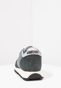 Baskets en suède et cuir gris avec un logo noir au talon, semelle intermédiaire blanche et semelle extérieure en caoutchouc noir texturé.