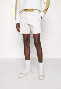 Vita shorts med elastisk midja, kombinerat med vita sneakers och ankelsockor. Outfiten har en mjuk, slät textur.