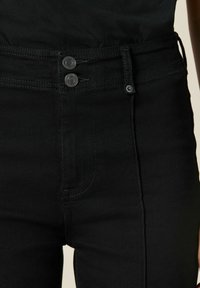 Čierne džínsy s vysokým pásom, vybavené dvoma kovovými gombíkmi, zipsom a tónovým prešívaním, vyrobené z denimu s hladkou textúrou.