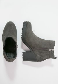 Stivaletti in suede grigi con tacco alto, zip laterale e suola in gomma testurizzata, caratterizzati da un bordo superiore leggermente curvo.