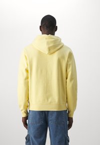 Felpa gialla in cotone con cappuccio regolabile, polsini e orlo a costine, e vestibilità rilassata, abbinata a pantaloni cargo in denim blu.