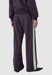 Paarse wijde trainingbroek van zacht materiaal met witte zijkanten. Heeft een comfortabele tailleband en een gladde textuur.