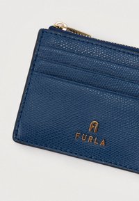 Blåt læderkortholder med tekstureret finish, der har flere kortholdere og et gyldent mærkelogo (FURLA) på forsiden. Lynlåskompartement inkluderet.