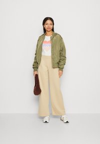 Olive green bomber jacket with ribbed cuffs, white t-shirt featuring a "love" graphic, beige wide-leg trousers, and brown fluffy handbag.