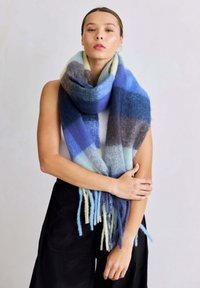 Multicolore wollen sjaal in tinten blauw en grijs, met een zachte textuur, franjes aan de randen en een geruit patroon.