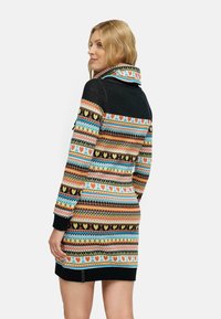 Knit dress dengan pola geometris berwarna-warni, dilengkapi dengan kerah cowl dan lengan hitam, menampilkan bentuk hati dan diamond.