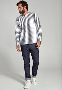 Langærmet stribet skjorte i hvid og marineblå, parret med mørkeblå jeans og hvide sneakers. Har en rund halsudskæring og oprullede ærmer.