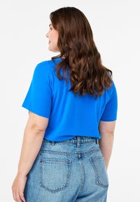 Hedvábně modrý top s krátkým rukávem, hladkou texturou, spárovaný s jeansy světle modré barvy s vysokým pasem, které mají zadní kapsy a volný střih.