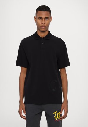 Polo noir avec un col, des manches courtes et trois boutons. Présente un logo texturé discret sur le devant. Tissu en coton lisse.
