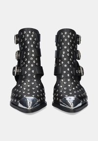 Botines negros de cuero con remaches circulares de plata y tres hebillas; punta metálica afilada con acabado espejado.
