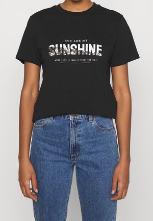 Schwarzes Baumwoll-T-Shirt mit weißem Text "DU BIST MEIN SONNENSCHEIN" und floralen Akzenten, kombiniert mit hochgeschnittenen blauen Jeans.