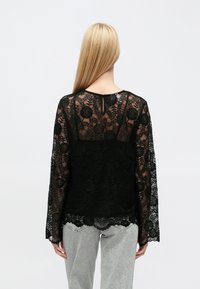 Juoda nėriniuota palaidinė su ilgomis rankovėmis, su gėlių raštais, scallop kraštu ir raktu formos iškirpte nugaroje. Medžiaga yra švelni.