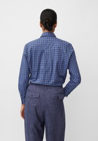 Camicia a maniche lunghe di colore blu con un motivo a griglia e colletto classico, abbinata a pantaloni viola testurizzati con tasche posteriori.