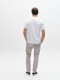 Camiseta blanca de manga corta, pantalones ajustados gris claro y zapatos negros. Figura masculina vista desde atrás sobre un fondo blanco liso.