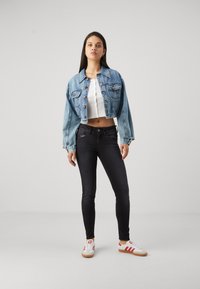 Light blue denim cropped jacket with button front, paired with a white cropped top and black skinny jeans. Footwear features red and white accents.