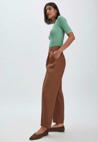 Lichtgroene ribbeltrui, bruine high-waisted broek met zijzakken en bruine ballerina's. Gladde textuur, recht model, minimale details.