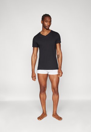 Schwarzes Kurzarm-V-Ausschnitt-T-Shirt, getragen mit weißen, enganliegenden Unterhosen, die einen glatten Stoff, ein einfaches Design und eine schlanke Passform zeigen.