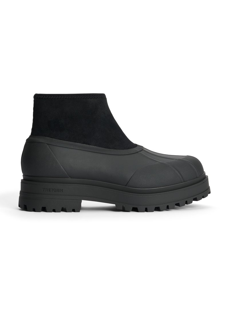 Mustat nilkkurit, joissa on teksturoitu kumista ja mokasta valmistettu yläosa, pyöristetty kärki ja paksu, uritettu pohja pitävää otetta varten.