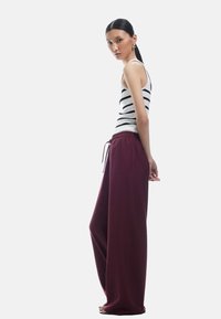 Haut sans manches à rayures associé à un pantalon large bordeaux. Tissu lisse et coupe décontractée ; le pantalon possède une taille élastique avec cordon de serrage.