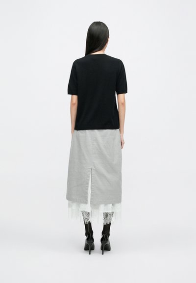 Μαύρη κοντομάνικη μπλούζα συνδυασμένη με γκρι φούστα με πίσω σκίσιμο και δαντέλα. Φοράει �μαύρες ψηλές μπότες.