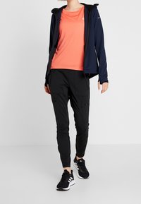 Námornická bunda na zip, jasně korálová košile, černé cargo kalhoty a černé sportovní boty. Tkanina se zdá být hladká a elastická.