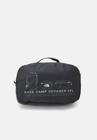 Czarna prostokątna saszetka z uchwytem, białe rysunki linii przedstawiające plecak i dwie torby, opisane jako "Base Camp Voyager 32L" oraz logo marki.