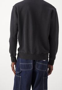 Černá mikina s dlouhými rukávy, žebrovanými manžetami a lemem. Nošena s modrými cargo kalhotami s kapsami a kontrastním švem.