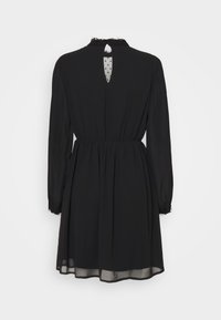 Robe noire à manches longues avec taille froncée, dos transparent à pois avec ouverture en forme de goutte et bordure en dentelle au col et aux poignets.