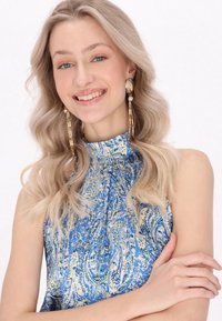 Rochie fără mâneci cu model albastru și galben, cu un gât înalt, asortată cu cercei lungi din aur și perle. Material fin cu un design fluid.