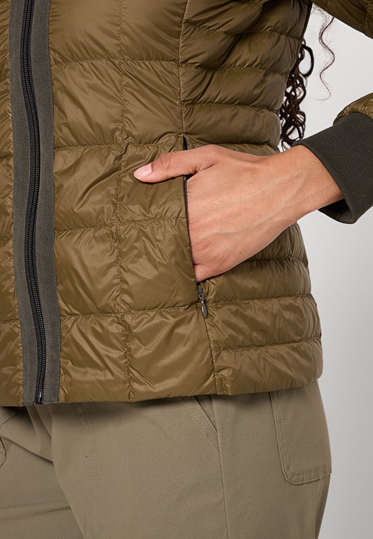 Olivgrüne Steppjacke mit einer Reißverschlusstasche, die eine strukturierte Oberfläche und dunkle Akzente aufweist. Verstellbare Bündchen in kontrastierender Farbe.