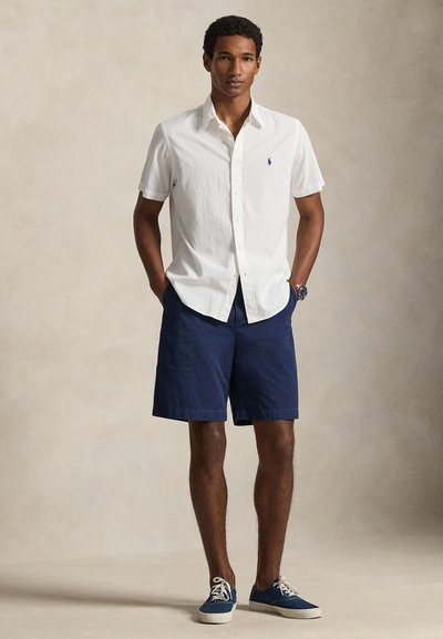 White short-sleeve button-up shirt, navy shorts, and navy sneakers; simple design with a textured shirt finish and classic styling.
