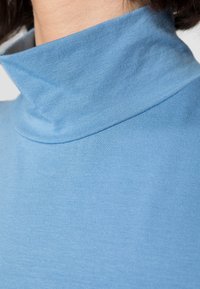 Light blue turtleneck top, made of soft ribbed fabric, featuring a high collar and fitted design. Smooth texture with minimal stitching details.