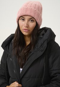 Giacca a vento nera con grande cappuccio, dotata di chiusura con zip. Completata da un berretto lavorato a maglia a coste di un delicato rosa pallido. Texture morbida e design casual.