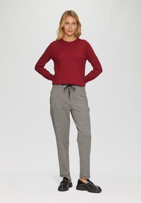 Rode trui met lange mouwen, gecombineerd met een broek met ruitpatroon. De broek heeft een elastische tailleband en een koord. Zwarte schoenen met dikke zolen.