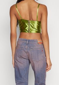 Top corto in satin verde con spalline sottili e zip sul retro, abbinato a jeans in denim chiaro e sbiadito con un patch sulla vita.