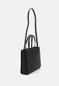 Černá obdélníková kabelka s vodorovnými polstrovanými pruhy, dvěma krátkými uchy a dlouhým nastavitelným ramenním popruhem na bílém pozadí.