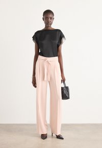 Top in satin nero con maniche corte, pantaloni palazzo rosa pallido con cintura a nodo e una piccola borsa nera testurizzata.