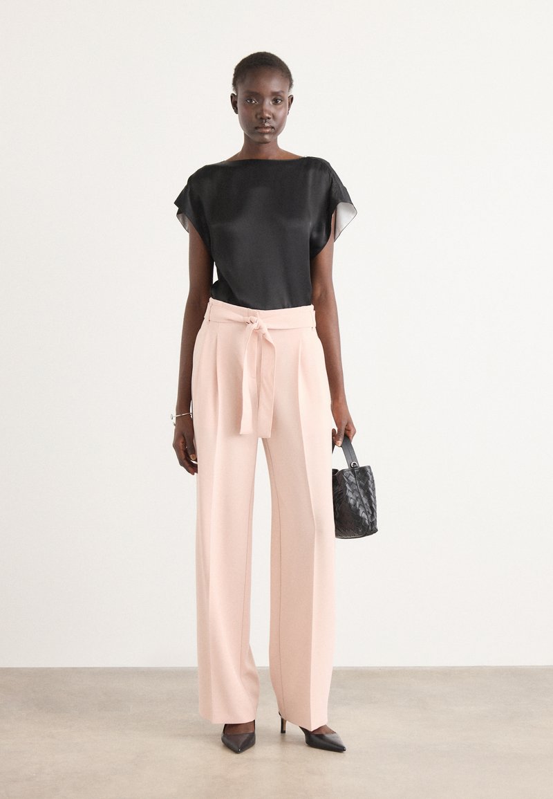 Top in satin nero con maniche corte, pantaloni palazzo rosa pallido con cintura a nodo e una piccola borsa nera testurizzata.