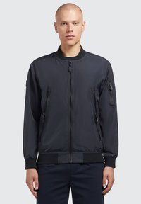 Tamno siva bomber jakna od glatkog, laganog materijala. Ima zatvarač sprijeda, rebrasti ovratnik i više džepova sa zatvaračem.