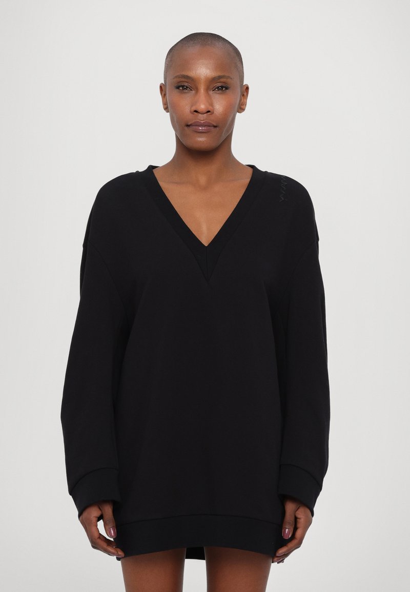 Robe-sweatshirt noire surdimensionnée avec un décolleté en V profond, des manches longues et des poignet en côtes. Texture lisse avec un minimum de détails de marque sur l'épaule.
