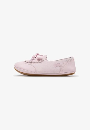 Chaussure d’enfant rose clair avec bords festonnés, un nœud sur le devant, texture suédée et semelle plate en caoutchouc marron, vue de profil.