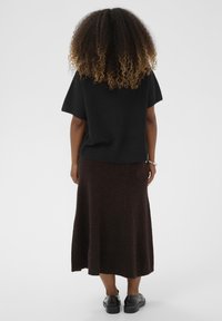 Black knit top with short sleeves paired with a dark brown, ankle-length skirt. Textured fabric, solid colors, and minimalist design featured.