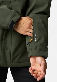 Grön vattentät jacka med texturerad finish, utrustad med elastiska ärmslut, justerbar dragsko och broderad STX 8000-logotyp.