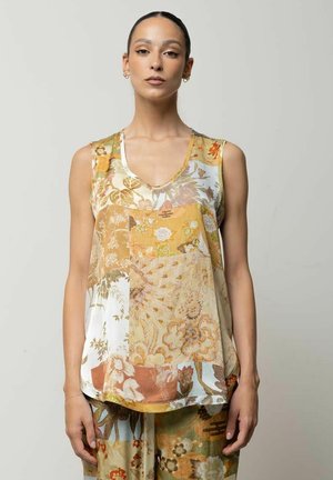 Donna che indossa un top patchwork floreale senza maniche e pantaloni floreali abbinati, in piedi davanti a uno sfondo grigio uniforme.