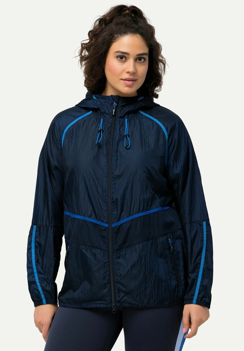 Marinblå vindjacka med kontrasterande blå detaljer, dragkedja fram och huva. Har strukturväv och dragkedjeförsedda sidofickor.