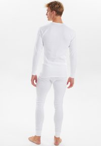 Hvid langærmet termisk top med rund hals og ribbede manchetter, parret med tætsiddende hvide termiske bukser. Glat tekstur, tætsiddende design.