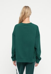 Felpa verde oversize con finitura testurizzata, colletto rotondo e spalle basse. I polsini e l'orlo a costine accentuano il taglio rilassato.